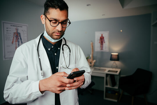 Mixed Race Male Nurse Texting On Cellular Device Standing In Clinic