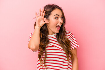 Fototapeta premium Young caucasian woman isolated on pink background trying to listening a gossip.