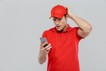 Young confused delivery man wearing uniform using mobile phone