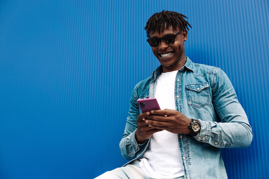 African Man Typing Sms On Blue Background, 5g Internet Concept, High Speed Internet On Phone