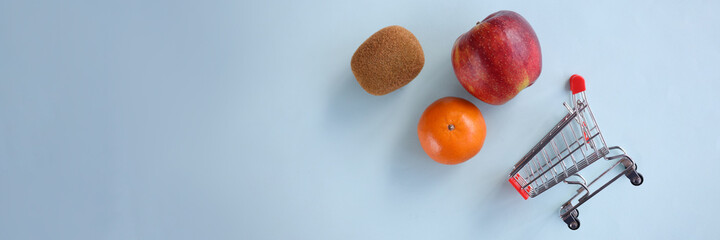 Fruits with a trolley from supermarket lie on blue background
