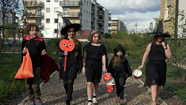 Group of children in black fancy dress with frightening make-up on their faces is running down the street. Halloween is a favorite children's holiday. Everyone is having a lot of fun.