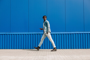 african guy walks with a phone around the city, against the background of a blue building, makes a...