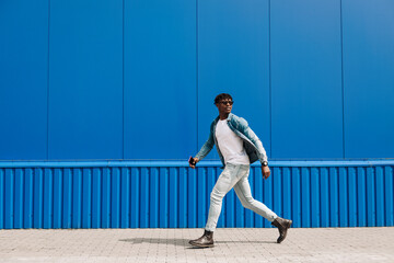 an african guy walks with a phone around the city, against the background of a blue building, makes a purchase online