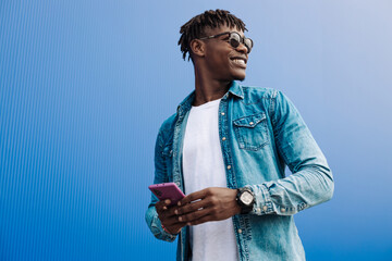 african man in sunglasses typing sms over blue background, 5g internet concept, high speed internet on phone