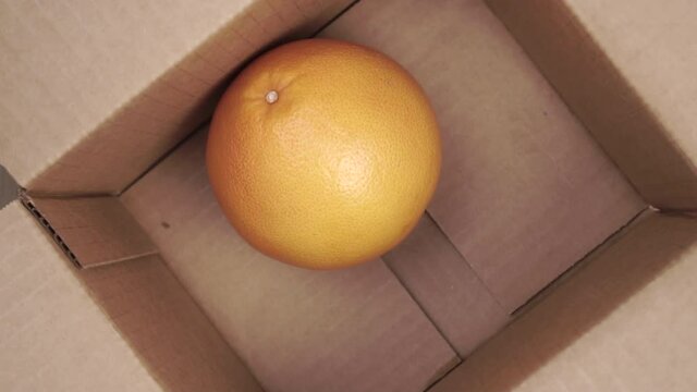Fresh citrus tropical pomelo fruit falls in slow motion into a cardboard shipping delivery box. Close up. Top view. Food online order concept. Packaging