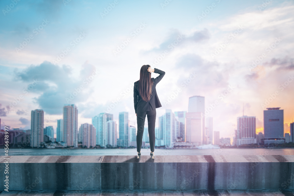 Poster back view of young female standing on concrete edge of building on city background with mock up plac