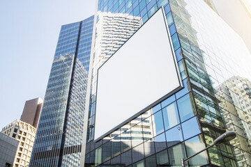 Empty white billboard on glass building in city with bright sky and daylight. Advertisement and...