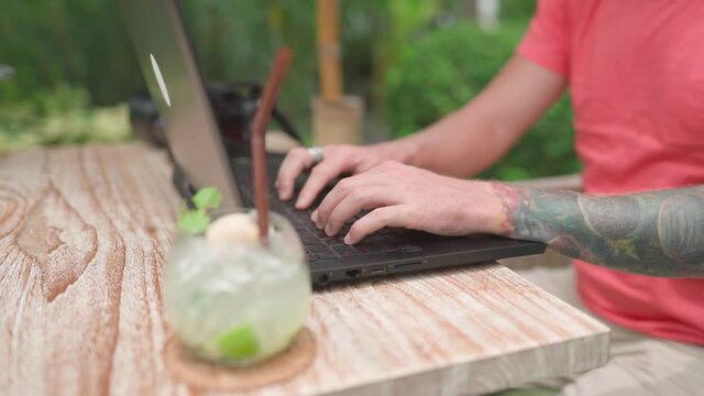 Man photogrpher in pink shirt working in outdoor cafe on laptop. Handheld shot