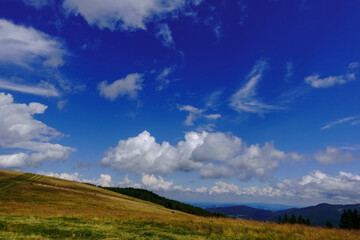 view view from a hilly mountain with grass to the valley and blue sky