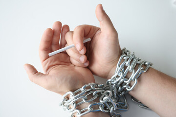 Male hands tied with metal chain holding cigarette on white background closeup