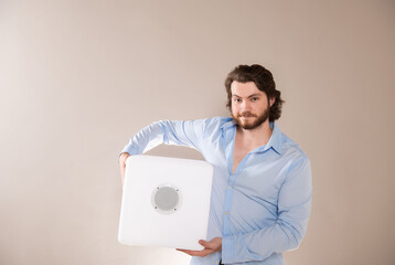 Young attractive man  holding white portable bluetooth speaker on gray background