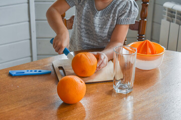 the child girl in the kitchen cuts and squeezes oranges juice