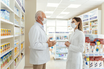 Fototapeta na wymiar Talking between two pharmacists and the corona virus. Before retiring, the pharmacist teaches the young pharmacist about working in a pharmacy. They wear uniforms and face masks