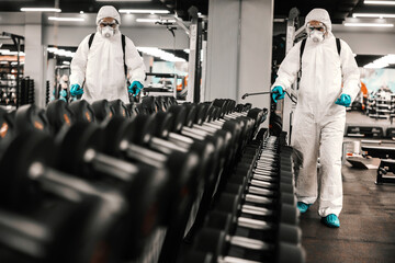 Expert in protective clothing cleans dumbbells and training equipment. Coronavirus concept, COVID19...