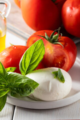 Principal ingredients of  Italian cousin,  mozzarella cheese, fresh tomatoes, basil herbs  and olive oil on white wood background