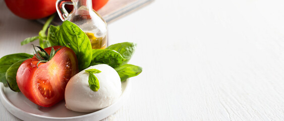 Italian cousin concept.Mozzarella cheese, fresh tomatoes, basil herbs  and olive oil on white plate.Large iname for  web banner,
