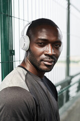 Portrait of African young athlete in wireless headphones looking at camera outdoors