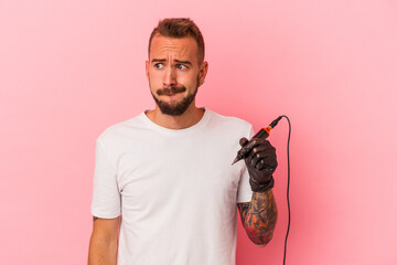 Young caucasian tattoo artist isolated on pink background  confused, feels doubtful and unsure.