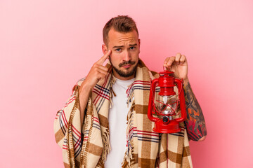 Young caucasian man with tattoos holding vintage lantern isolated on pink background  pointing temple with finger, thinking, focused on a task.
