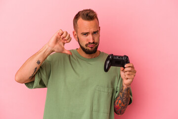 Young caucasian man with tattoos holding game controller isolated on pink background  feels proud and self confident, example to follow.