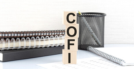 COFI text on wooden block with notebooks on white background