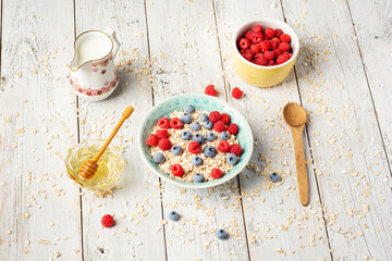 Oatmeal porridge with fresh raspberry and blueberry on bright white background. Healthy breakfast...