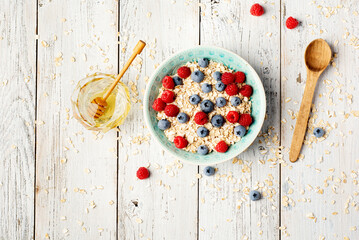 Oatmeal porridge with fresh raspberry and blueberry on bright white background. Healthy breakfast for children and parents. Tasty vegetarian food.