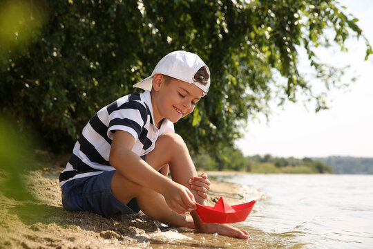 Cute little boy playing with paper boat near river