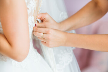 Obraz na płótnie Canvas The bridesmaid prepares the bride for the wedding day, helps to button her dress