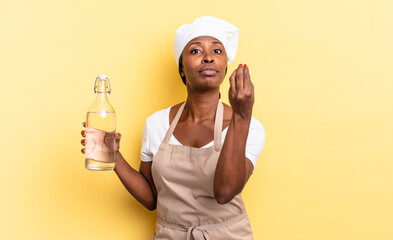 black afro chef woman making capice or money gesture, telling you to pay your debts! holding a...