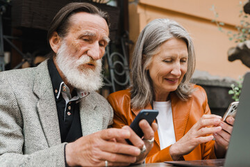 White senior couple using gadgets while sitting in cafe