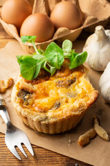 Top view of mushroom quiche with lamb's lettuce, garlic, eggs and fork, selective focus, on wooden table, black background, vertical