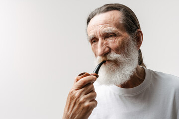 European senior man looking aside while posing with smoking pipe