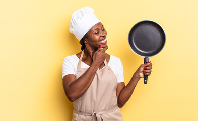 black afro chef woman smiling with a happy, confident expression with hand on chin, wondering and...