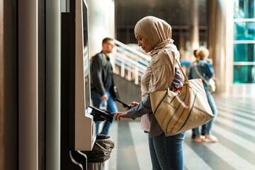 Woman in hijab using mobile phone while buying ticket at station