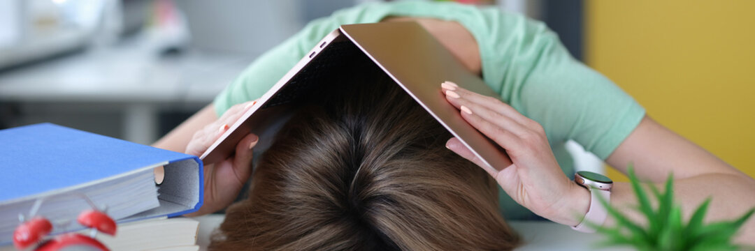Tired young woman lies on table on head with laptop - Powered by Adobe