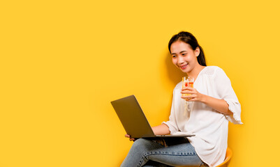 Asian woman drinking beer and is working on his laptop computer. and a happy smile happy work concept on a yellow background in the studio
