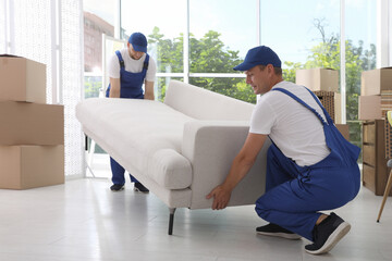 Moving service employees carrying sofa in room