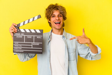 Young caucasian man with makeup holding clapperboard isolated on yellow background  person pointing...