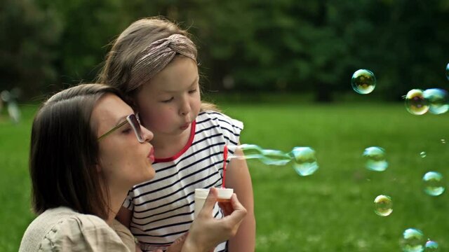 Young woman and her 6 year old daughter are blowing rainbow soap bubbles. Fun family vacation.