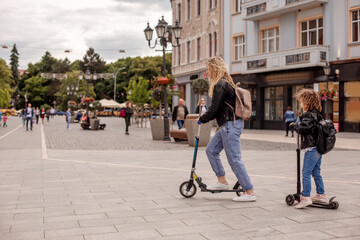 The stylish young mom and daughter are riding scooters