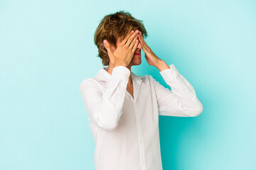 Young caucasian man with make up isolated on blue background  afraid covering eyes with hands.