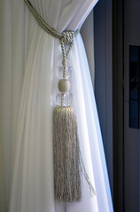 Drapery white curtain tied with a large weave rope. Interior Of Living Room ray curtain tied with Luxury tie back, rope in living room. Window with beautiful decorative ties from textiles for curtains