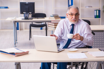 Old male employee in wheel-chair drinking coffee during break