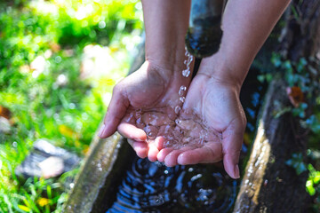 Agua de una fuente de montaña cayendo en manos de mujer.