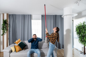 Young couple stares at the ceiling and yells because a neighbor upstairs is having a party with loud music or renovating an apartment and workers are drilling with heavy tools - obrazy, fototapety, plakaty