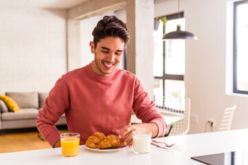 Young mixed race man eating croissant in a kitchen on the morning