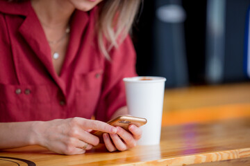 young woman in a red dress with a phone and cup of coffee sits at a table in a cafe