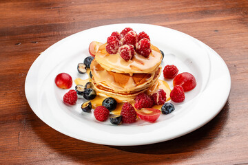 Pancakes with caramel and seasonal berries on a wooden backdrop. Breakfast